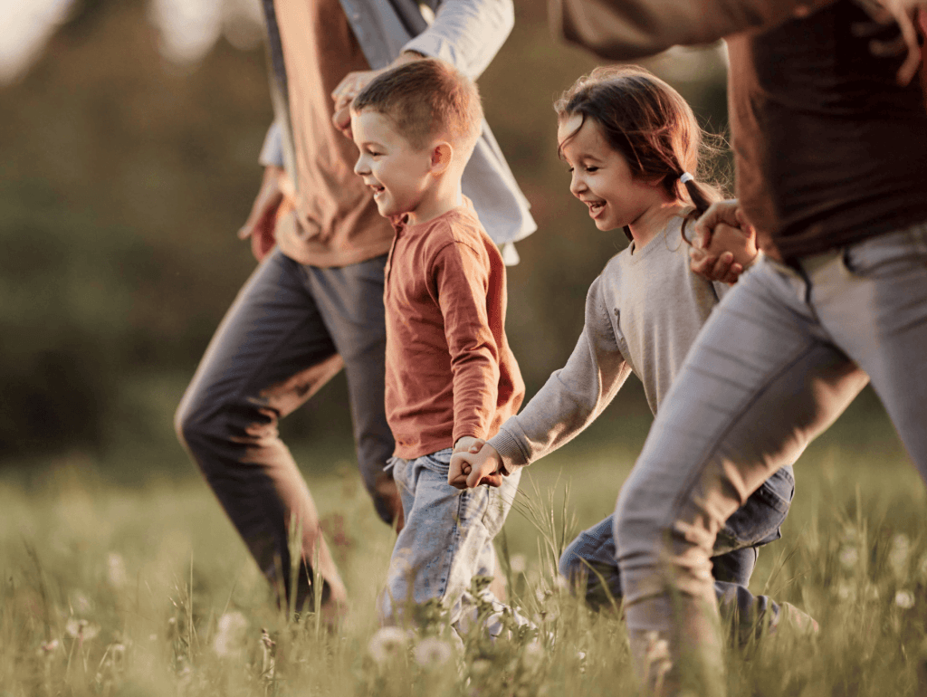 Children running through field holding hands with parents.